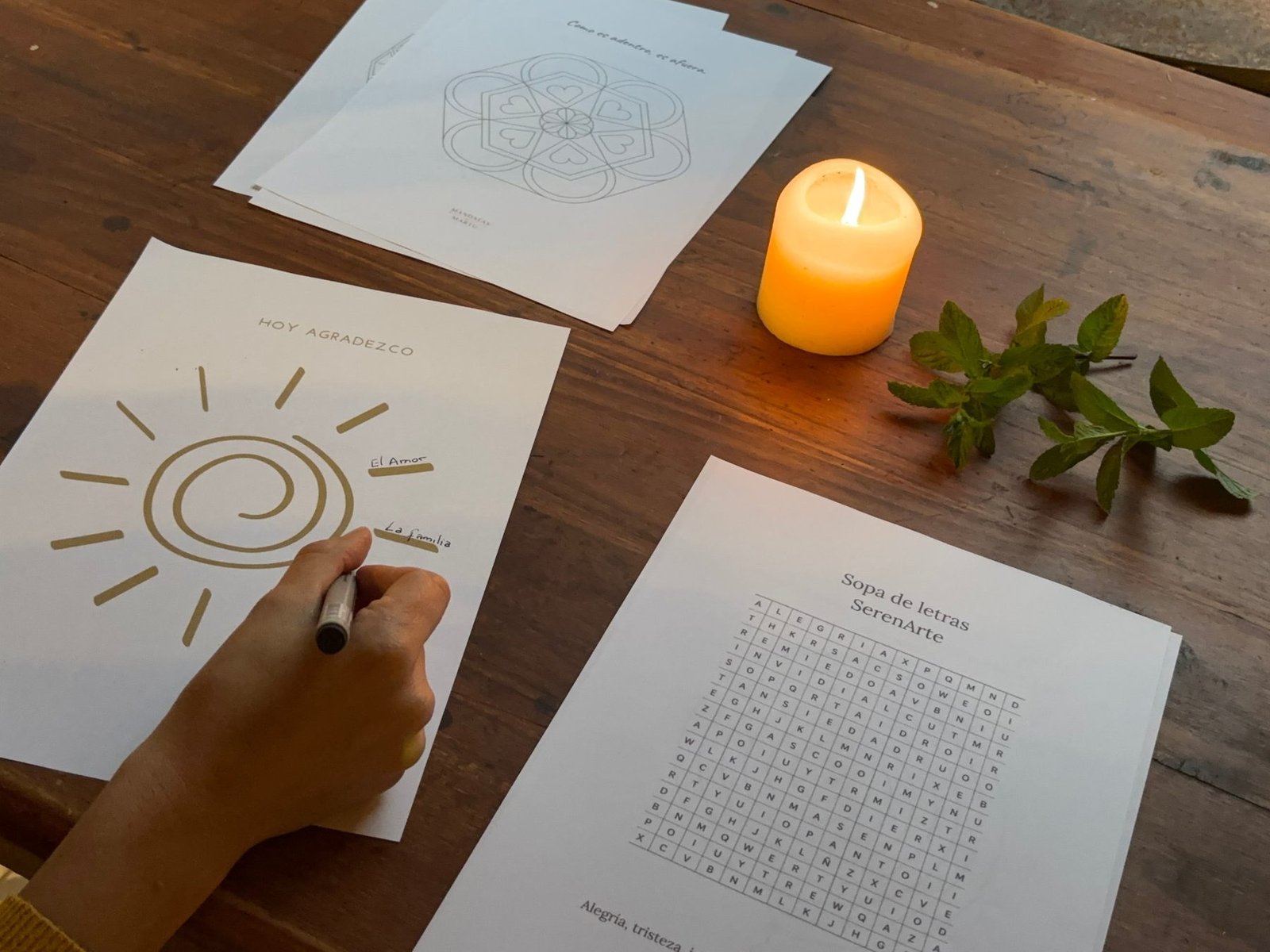 Hojas de Ideas SerenArte sobre la mesa: un mandala, «Hoy agradezco» y la sopa de letras, junto a una vela y menta